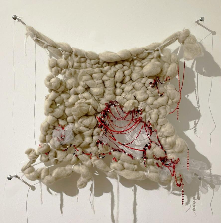 Mujeres — obra textil de vellón blanco atravesada por hilos rojos